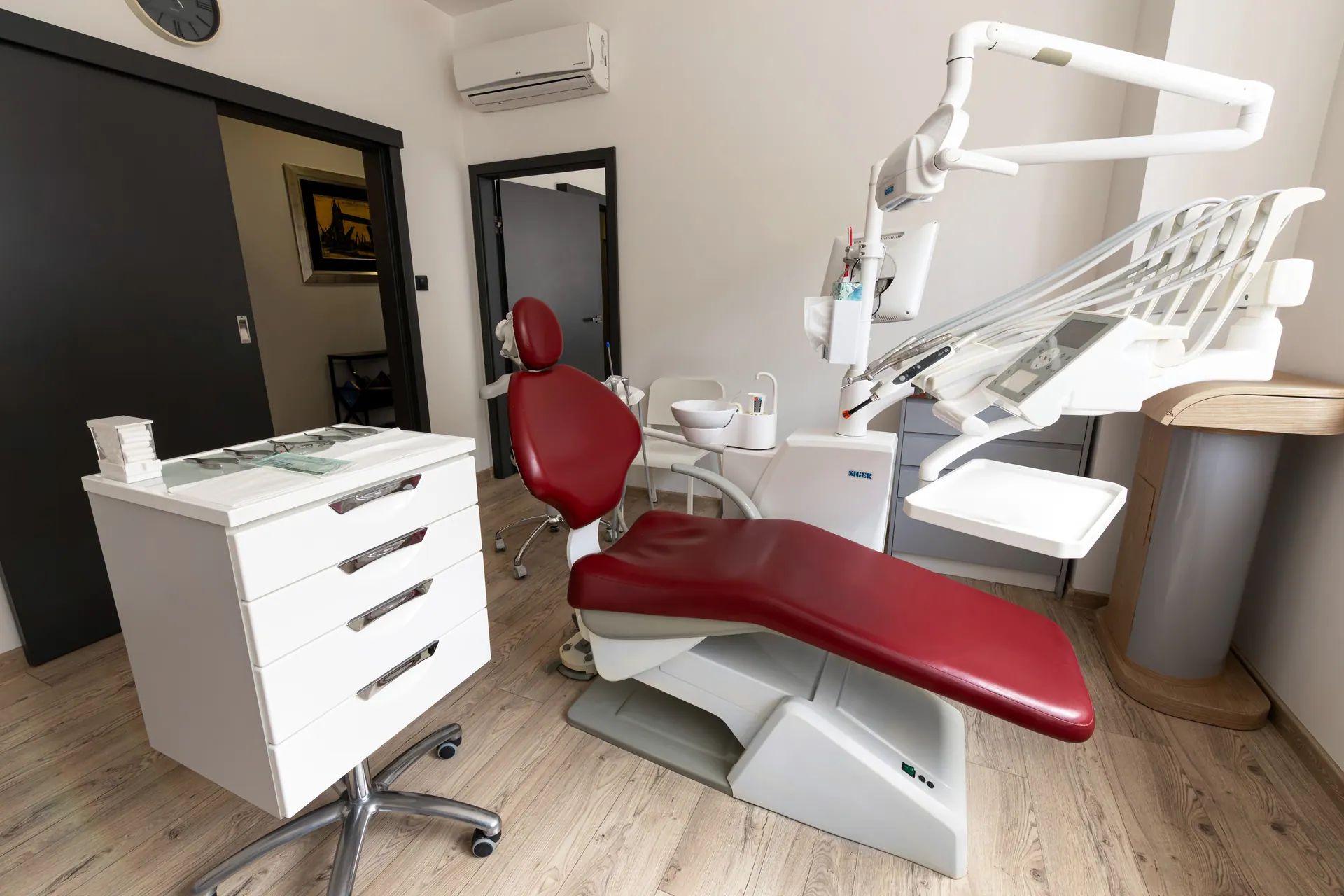 Sala zabiegowa Orto-vis z bordowym fotelem i nowoczesnym unitem stomatologicznym.