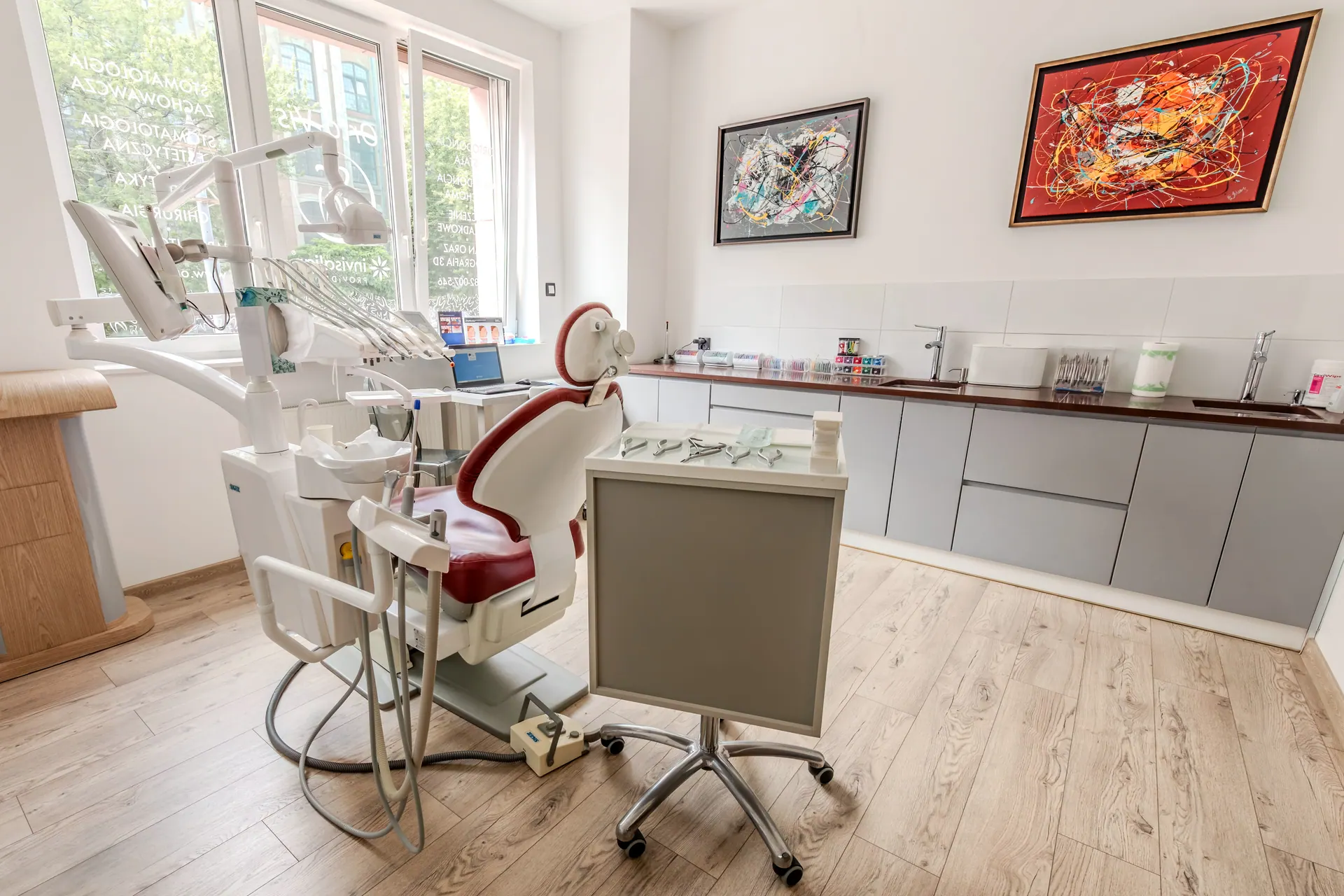 Przestronna sala zabiegowa Orto-vis z szafkami, unitem i widokiem na zieleń.